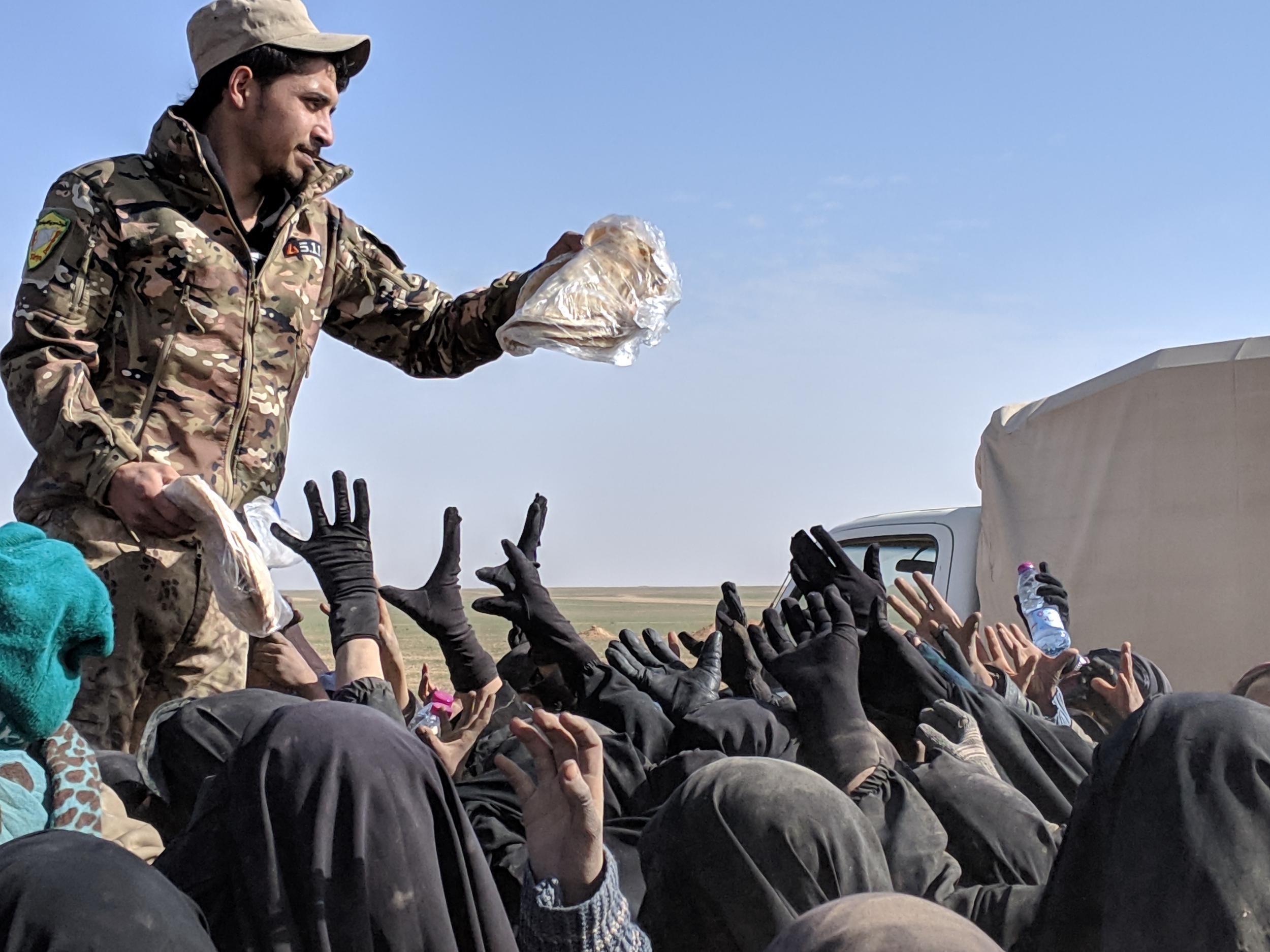 An SDF fighter hands out bread to the newly arrived families