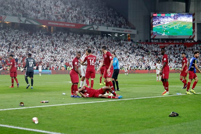 Qatar's Salem Al Hajri lies on the pitch after shoes and bottles were thrown
