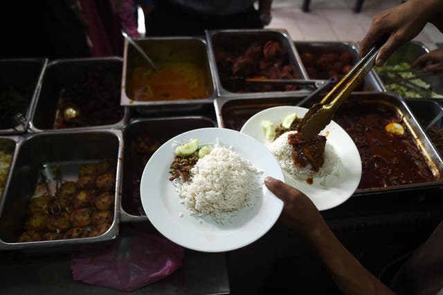In this picture taken 25 March, 2015 a Malaysian stall assistant serves Nasi Lemak dish on a plate at the Nasi Lemak Tanglin stall in Kuala Lumpur.