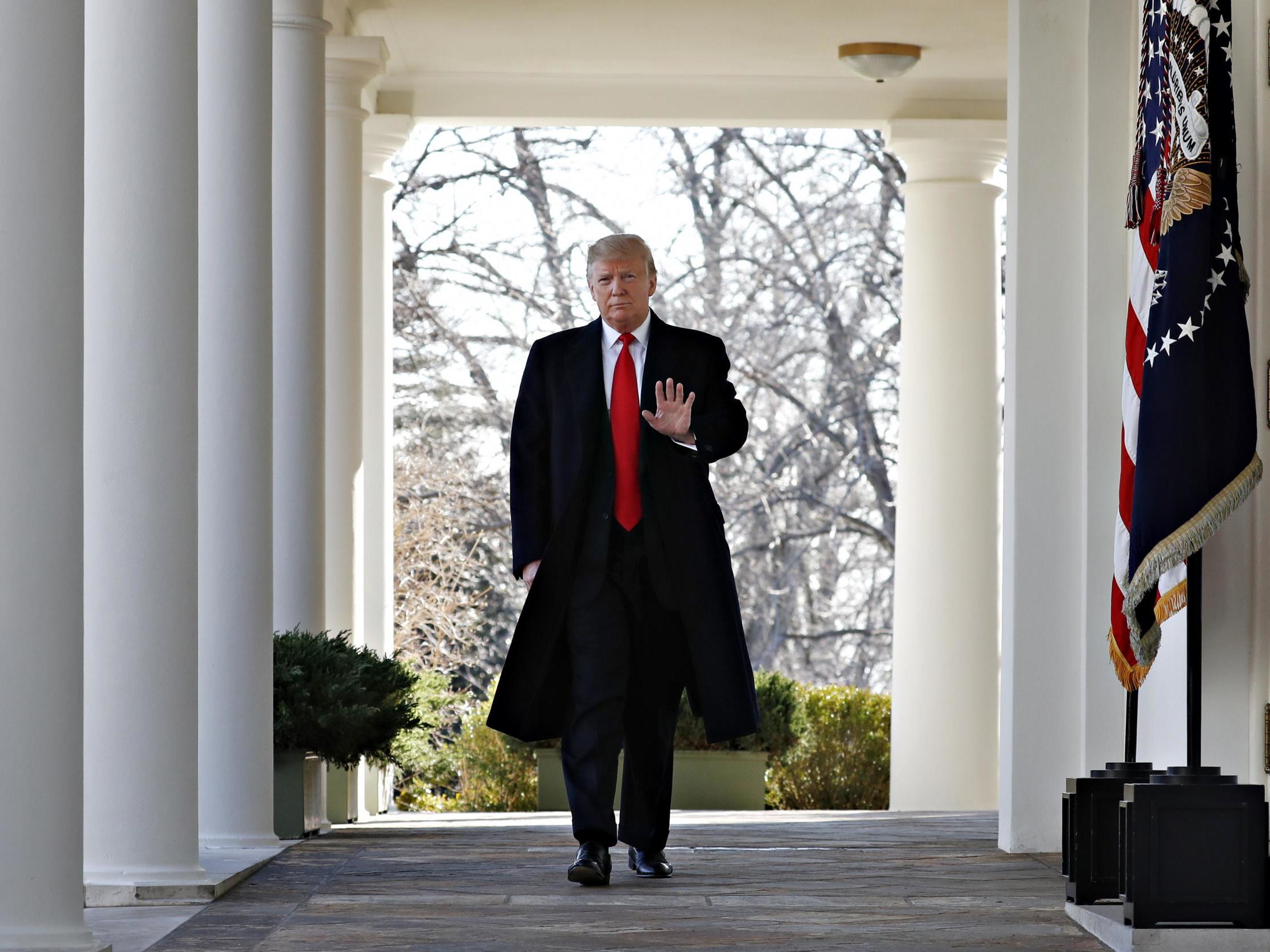 President Donald Trump waves as he walks through the Colonnade from the Oval Office of the White House