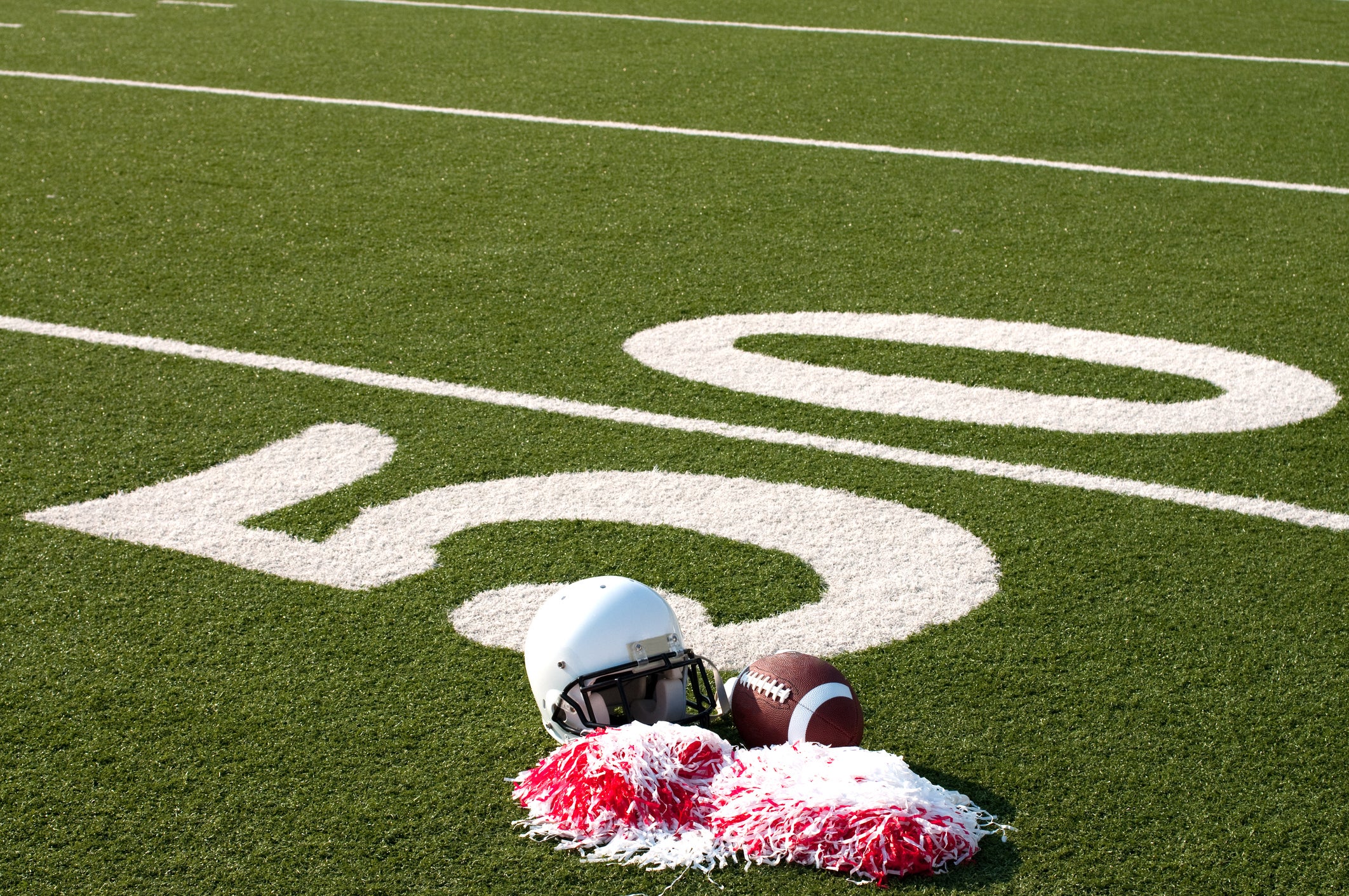 American football, helmet, and pom poms on field next to 50 yard line.