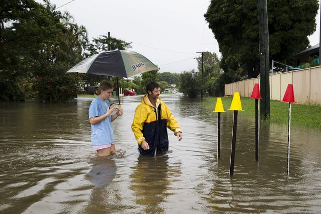 Local resident Paul Shafer and his daughter Lily stand in floodwaters near star pickets that show where the storm water cover has been removed