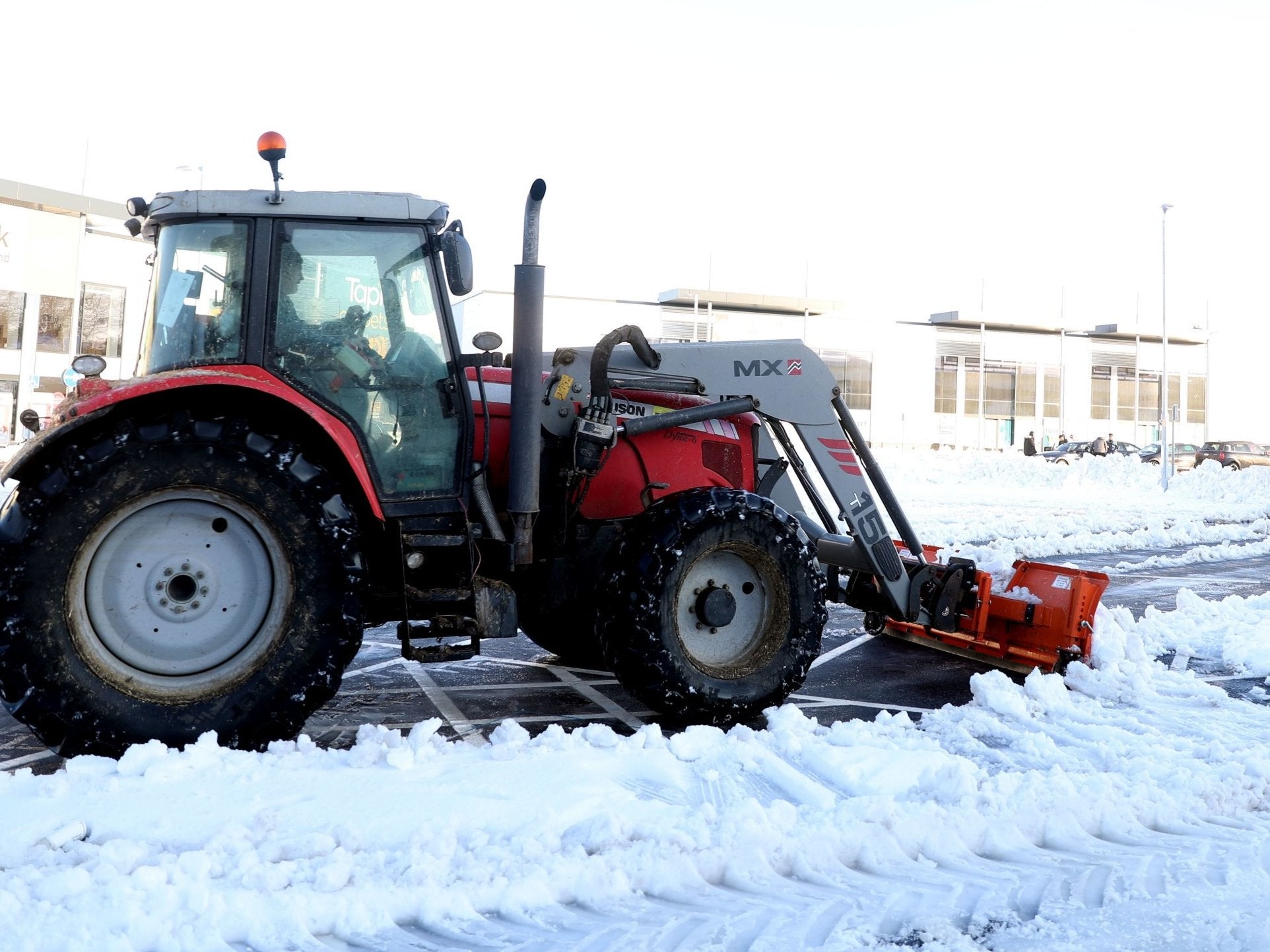 A tractor with a snow plough clears snow at a shopping park in Basingstoke