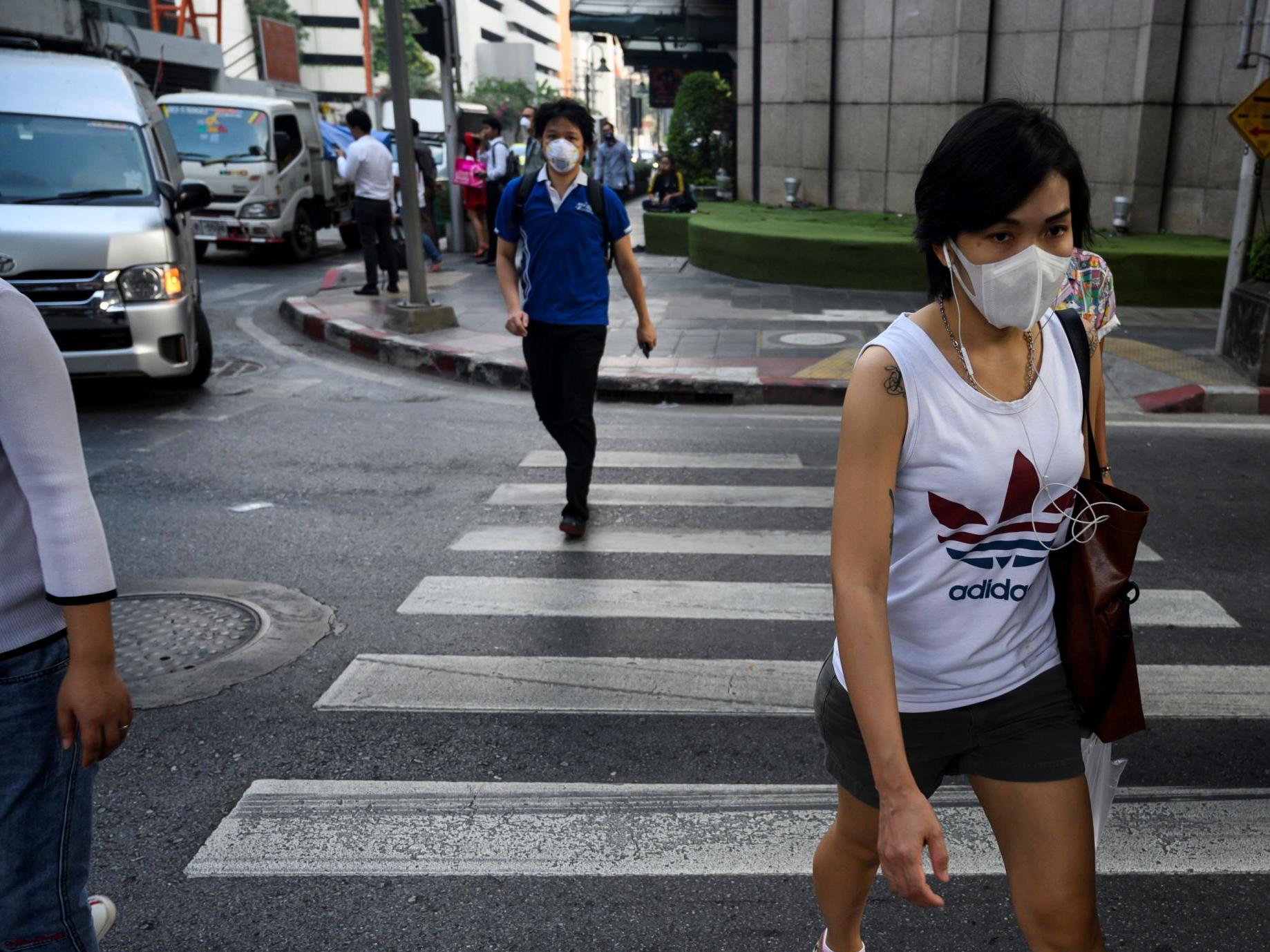 People, wearing face masks, make their way along a street in Bangkok