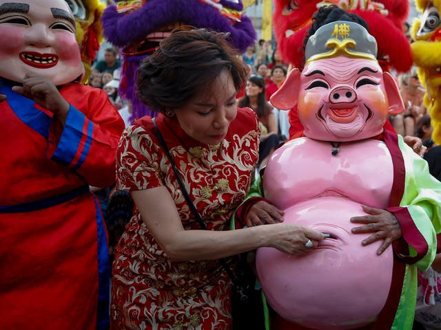 A woman puts money inside the belly of a performer in pig costume during a performance to celebrate the Lunar New Year in Chiantown in Bangkok, Thailand