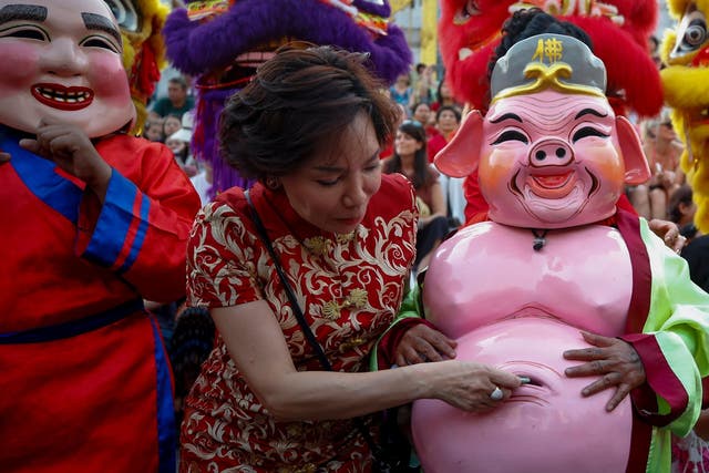 A woman puts money inside the belly of a performer in pig costume during a performance to celebrate the Lunar New Year in Chiantown in Bangkok, Thailand