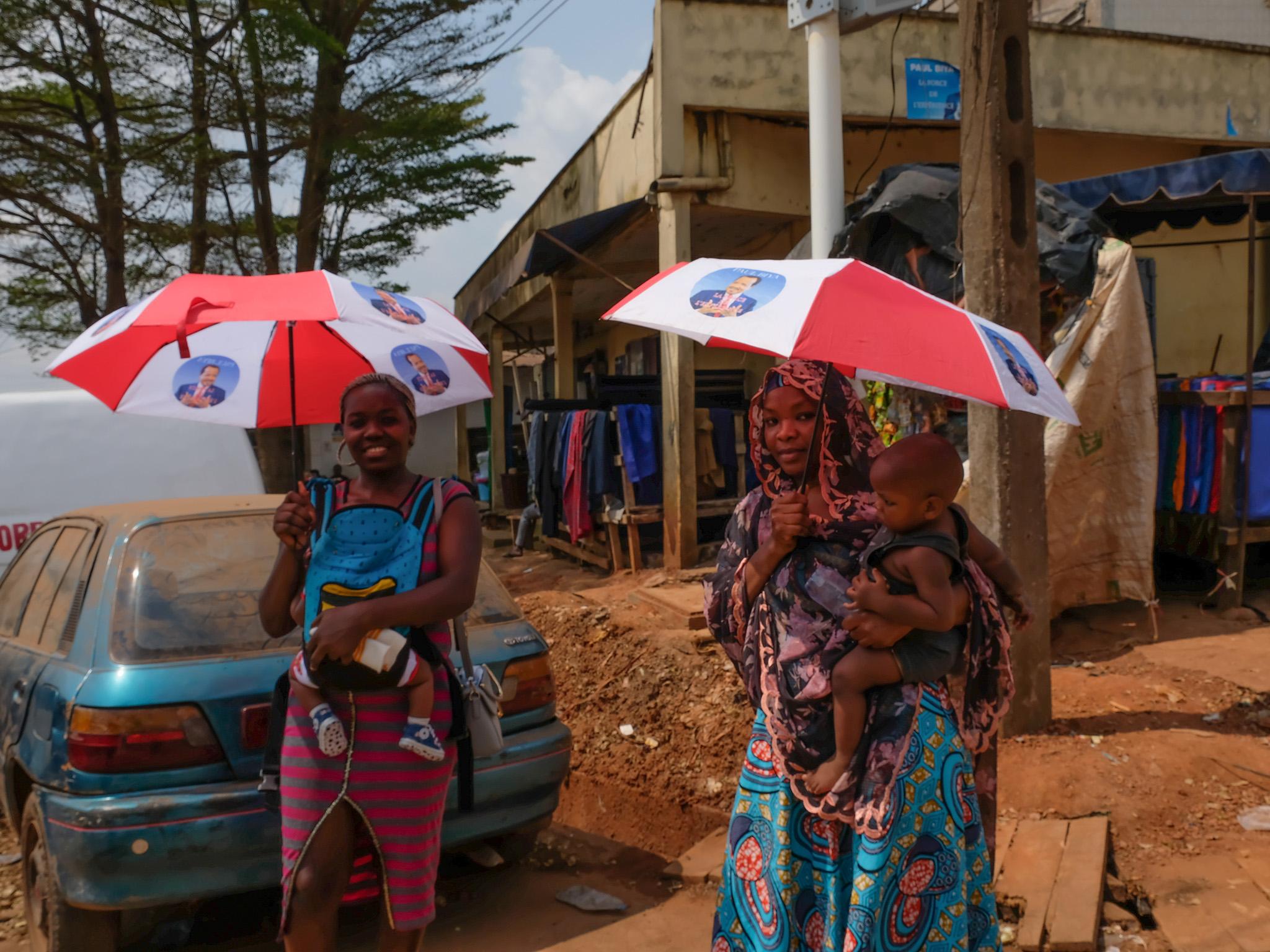 Women in Yaounde, Cameroon, carry umbrellas they received as campaign handouts featuring Paul Biya, president since 1982