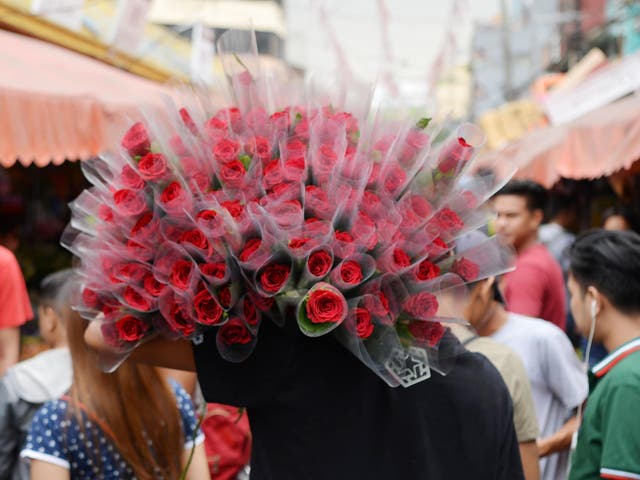 A vendor carries roses for sale along a street a day before Valentine's day