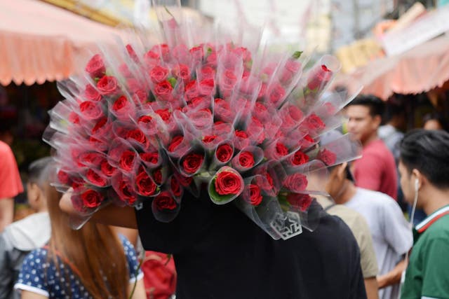 A vendor carries roses for sale along a street a day before Valentine's day
