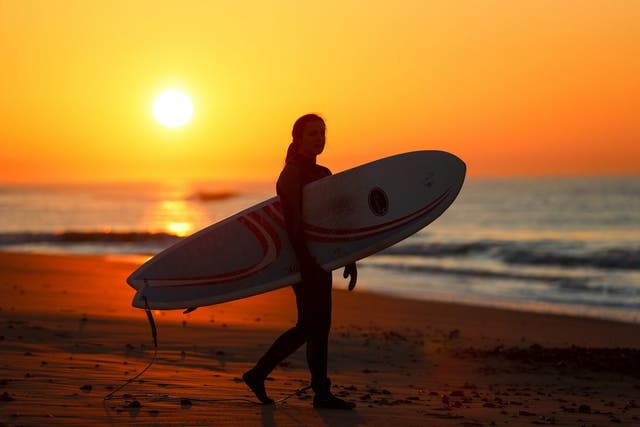 A surfer makes their way to the sea during sunrise at Boscombe beach in Dorset as Britain could experience more record-breaking temperatures this week after Monday became the warmest winter day on record