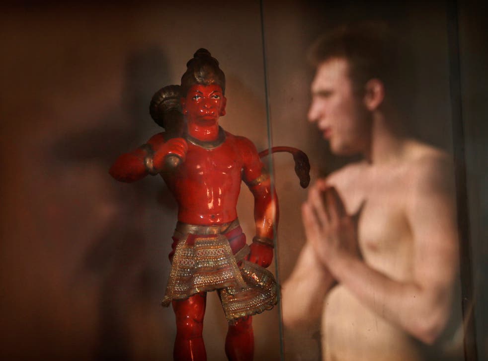 A man folds his hand in reverence at a statue of the Hindu monkey-god Hanuman