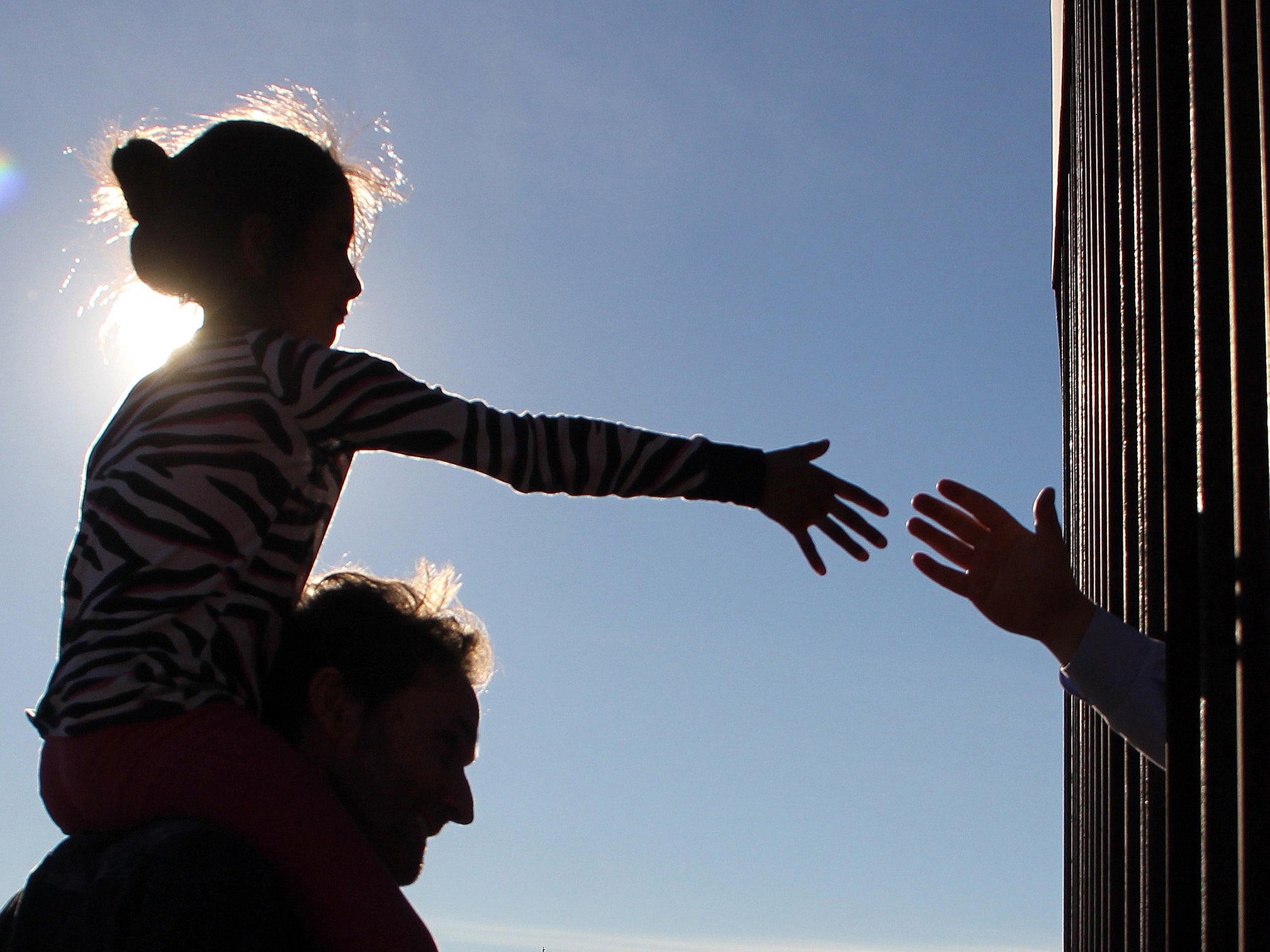 A girl from Anapra, a neighbourhood on the outskirts of Ciudad Juarez in Mexico, touches hands with a person in the US through the border fence (AFP/Getty)