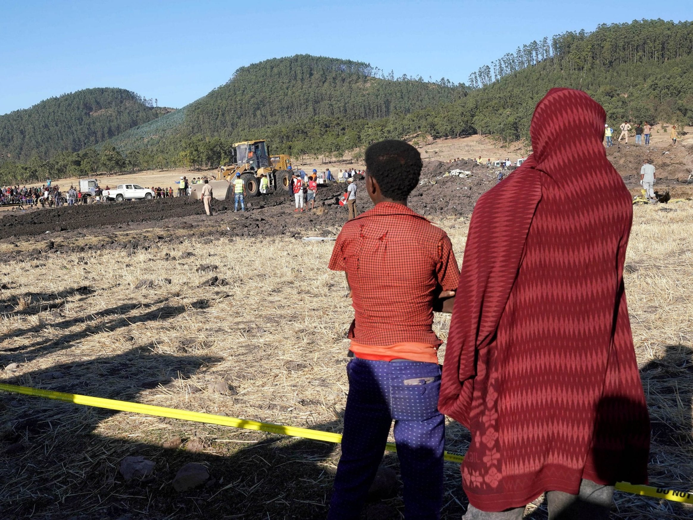 Residents watch as rescuers use an earth mover to recover debris from the field where Ethiopian Airlines Flight 302 crashed