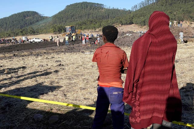 Residents watch as rescuers use an earth mover to recover debris from the field where Ethiopian Airlines Flight 302 crashed