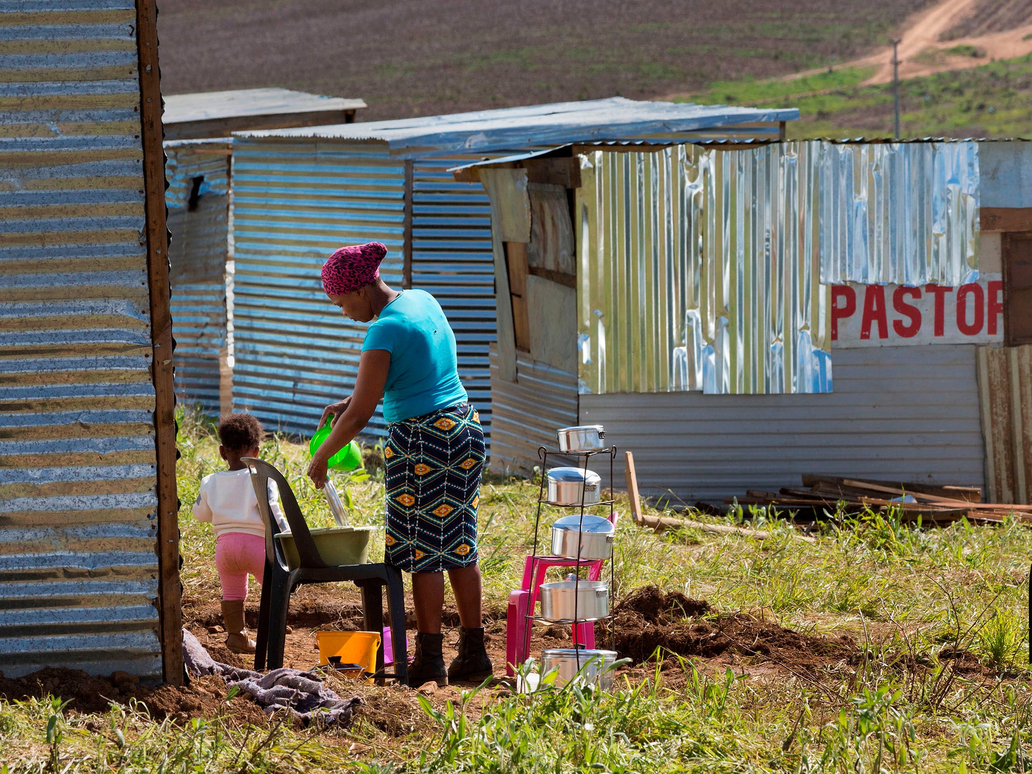 A woman washes her dishes outside her recently-built shack on a piece of land belonging to the Louiesenhof Wine Estate