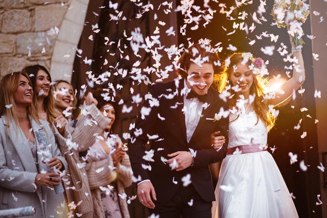 Newlywed husband and wife walking out of church and celebrating marriage with guests throwing confetti
