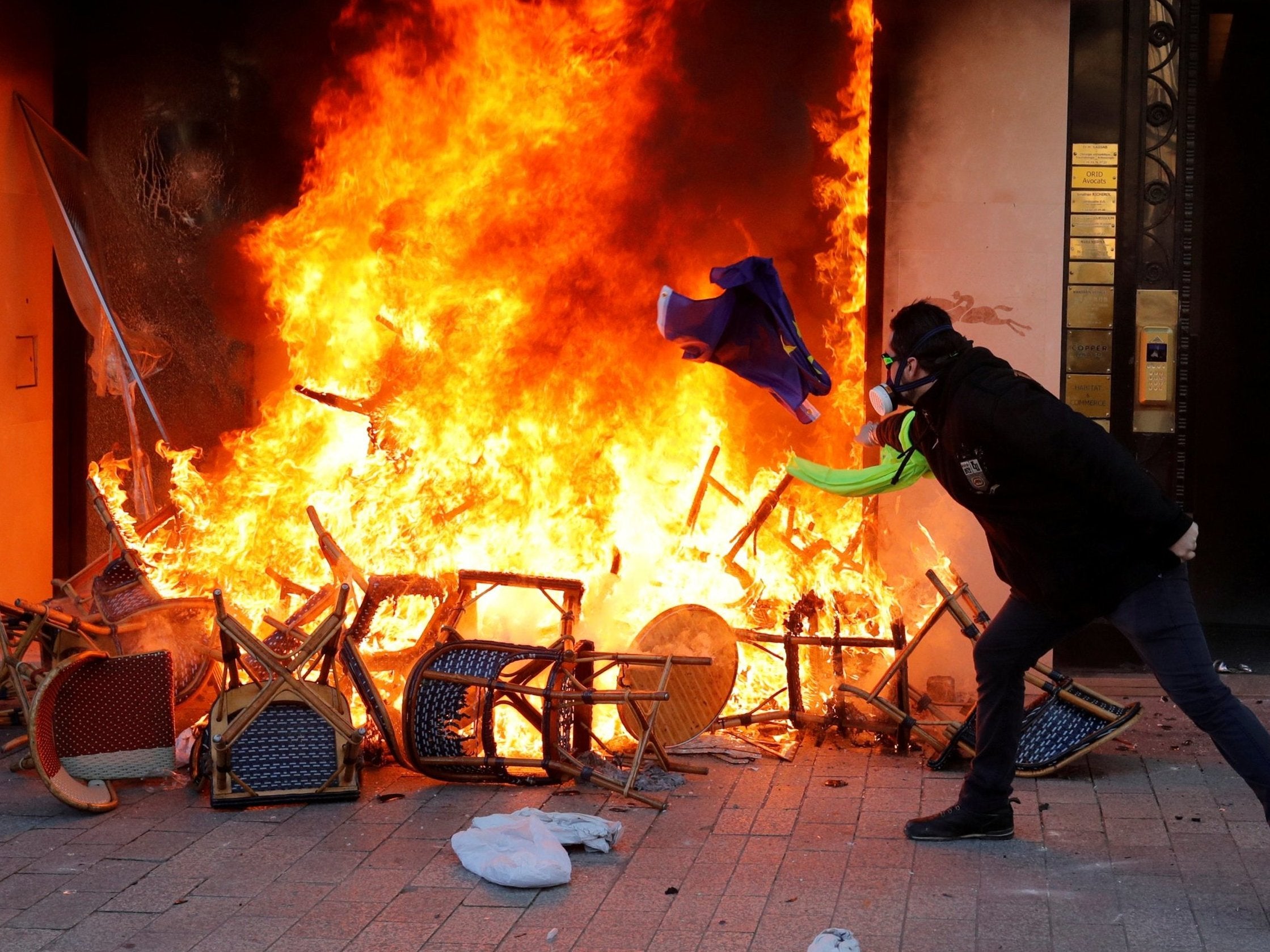 A protester throws a flag into the fire of a burning shop during Saturday's riots