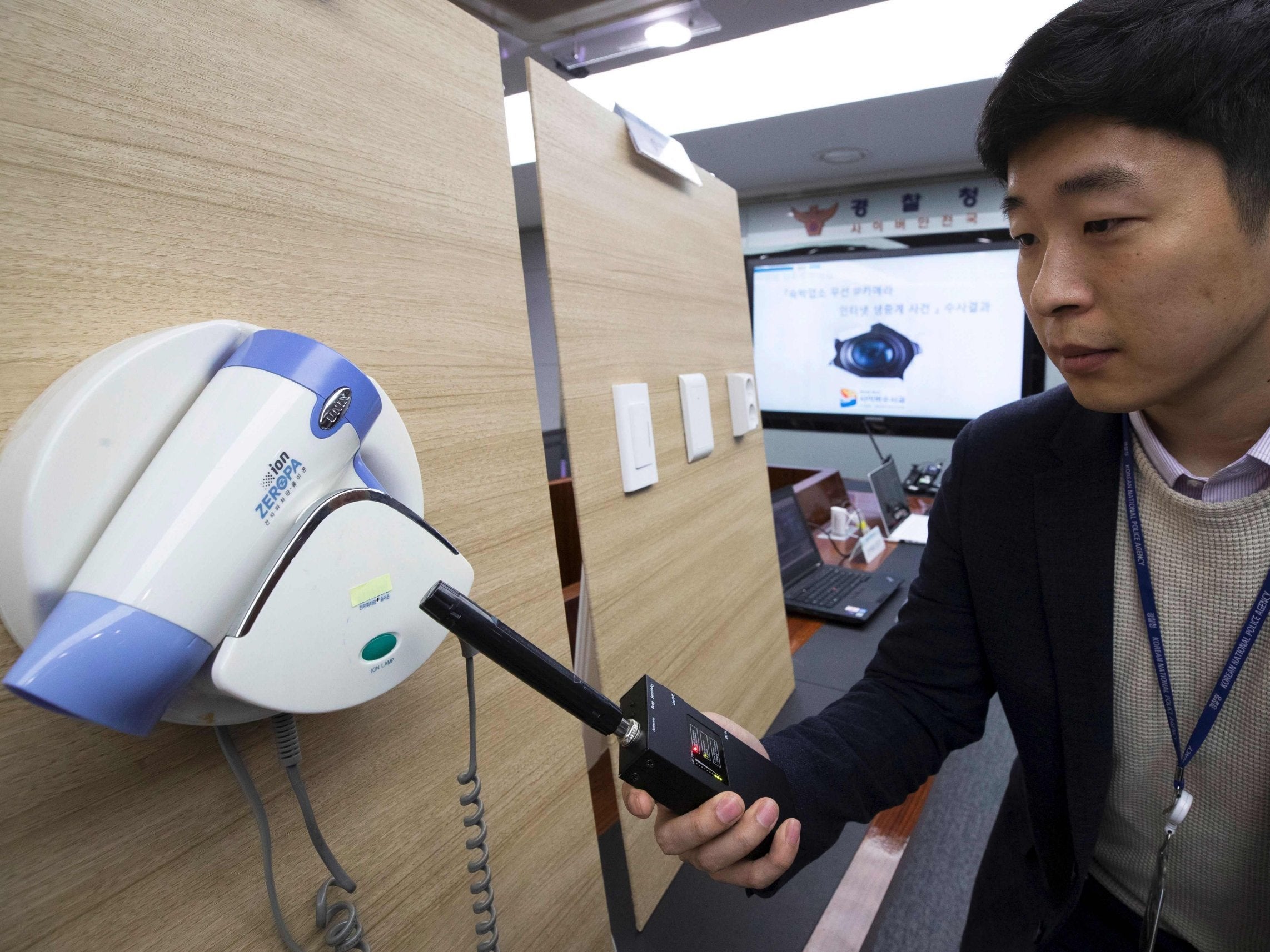 A police official waves a spy-cam detector in front of a wall-mounted hairdryer during a press conference in Seoul