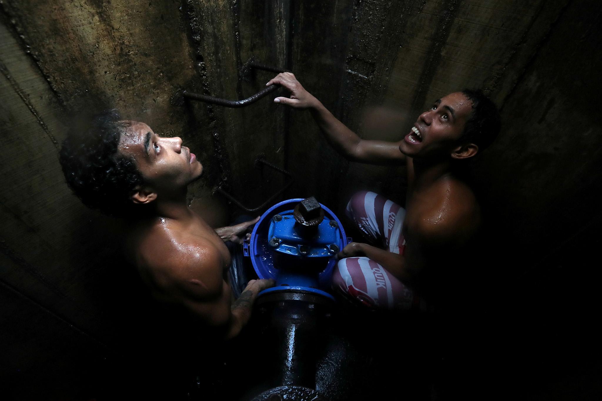 Locals collect water from an underground mains line in Caracas, Venezuela