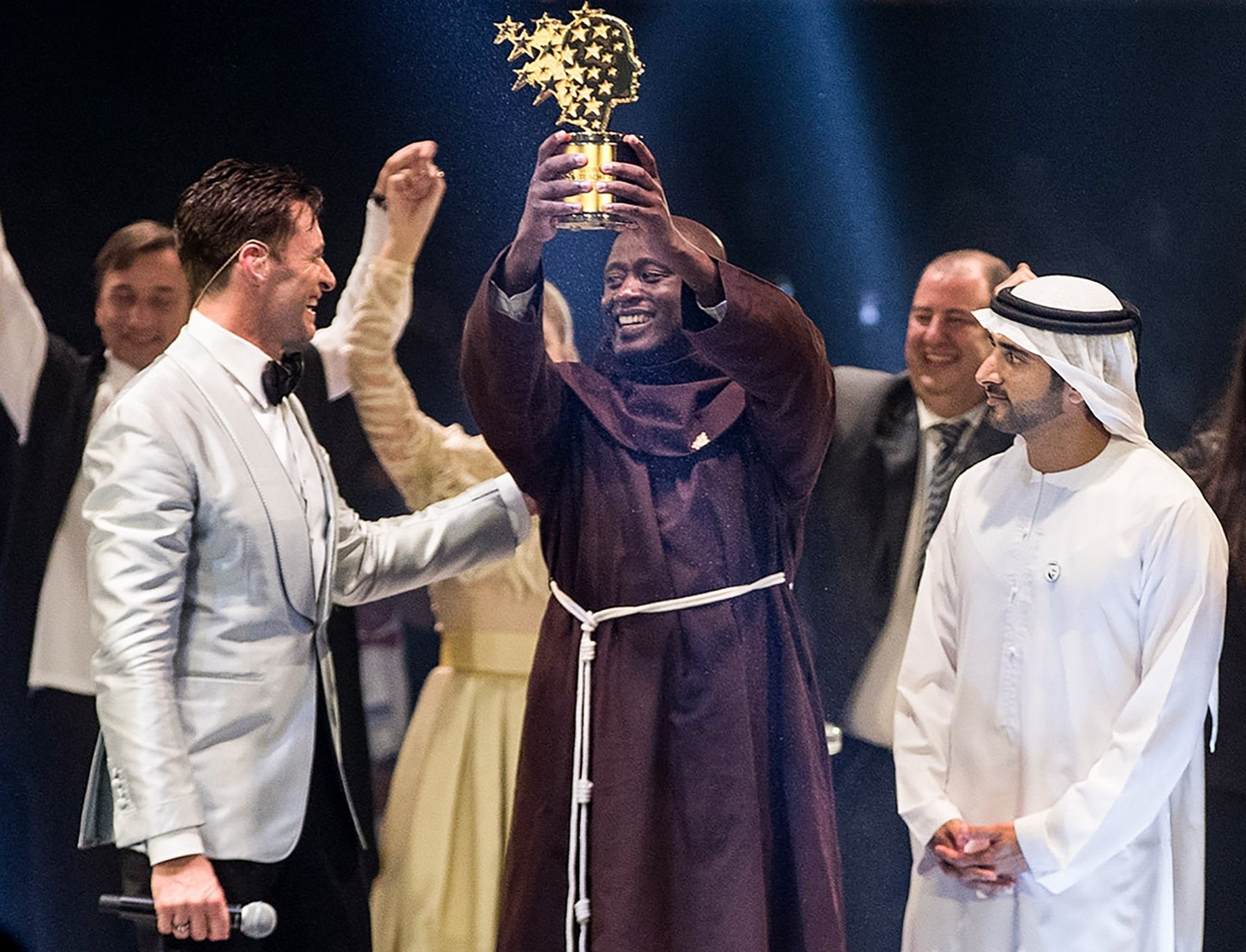 Peter Tabichi is given the Global Teacher Prize trophy by actor Hugh Jackman, left, and Dubai Crown Prince Hamdan bin Mohammed Al-Maktoum, right