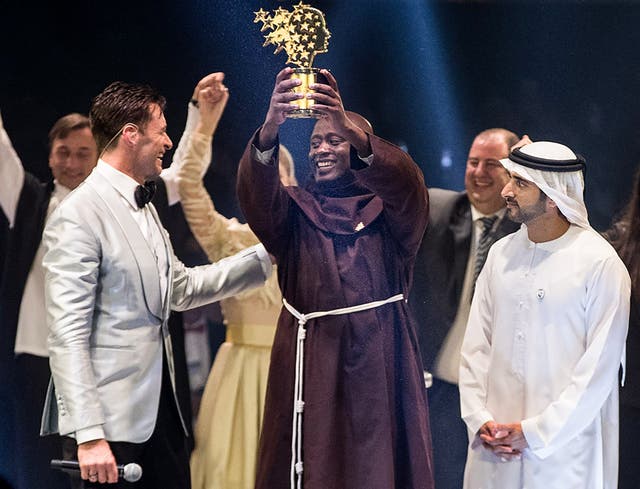 Peter Tabichi holds up the Global Teacher Prize trophy after winning the $1m award during a ceremony in Dubai presented by Australian actor Hugh Jackman, left, and Dubai Crown Prince Hamdan bin Mohammed Al-Maktoum, right