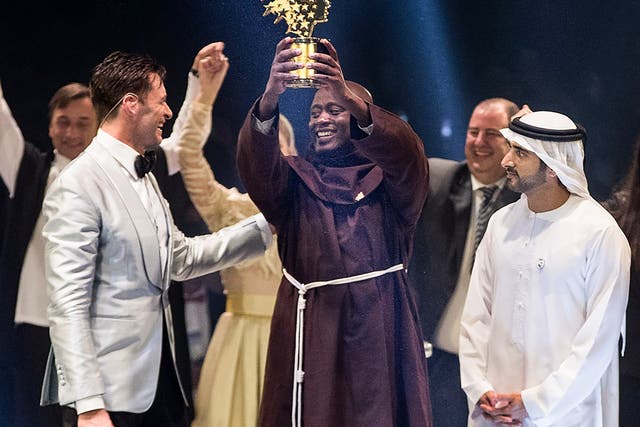 Peter Tabichi holds up the Global Teacher Prize trophy after winning the $1m award during a ceremony in Dubai presented by Australian actor Hugh Jackman, left, and Dubai Crown Prince Hamdan bin Mohammed Al-Maktoum, right
