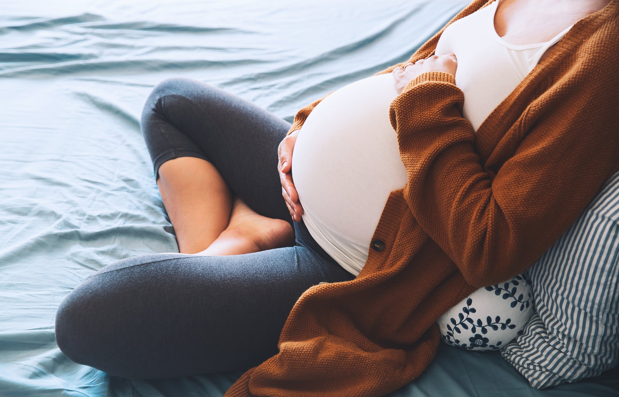 Pregnant woman sitting at bed and holds hands on belly in bedroom at home. (Getty Images/iStockphoto)