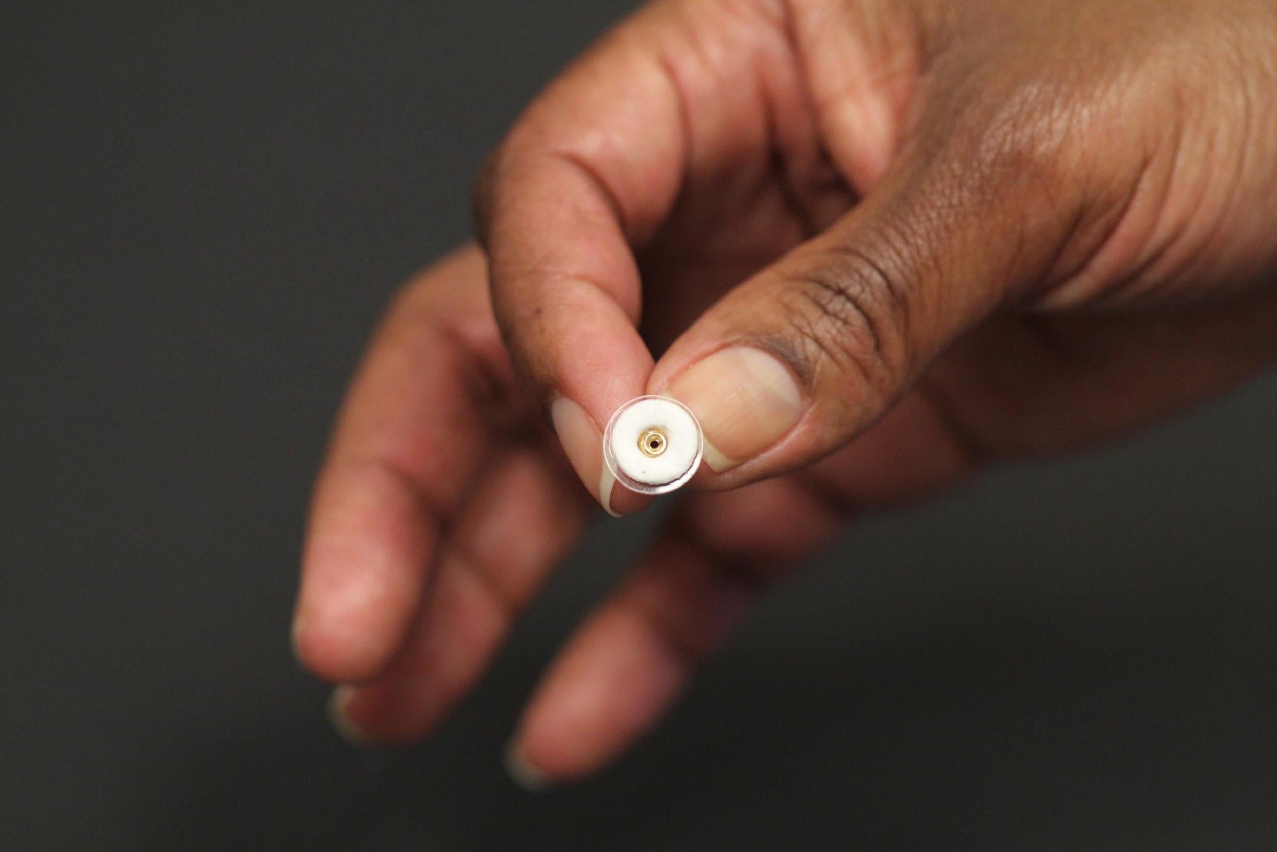 This photograph shows an earring patch (white) that can deliver contraceptive hormone while being worn on an earring back