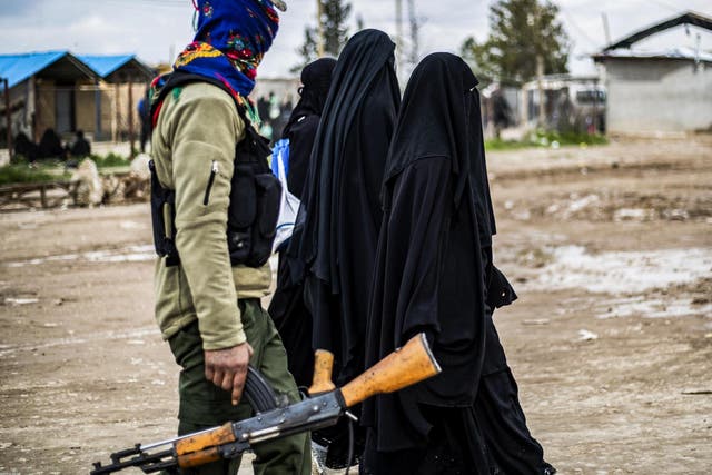 Foreign women living in al-Hol camp, which houses relatives of Isis members, walk under the supervision of a fighter of the Syrian Democratic Forces on 28 March 2019