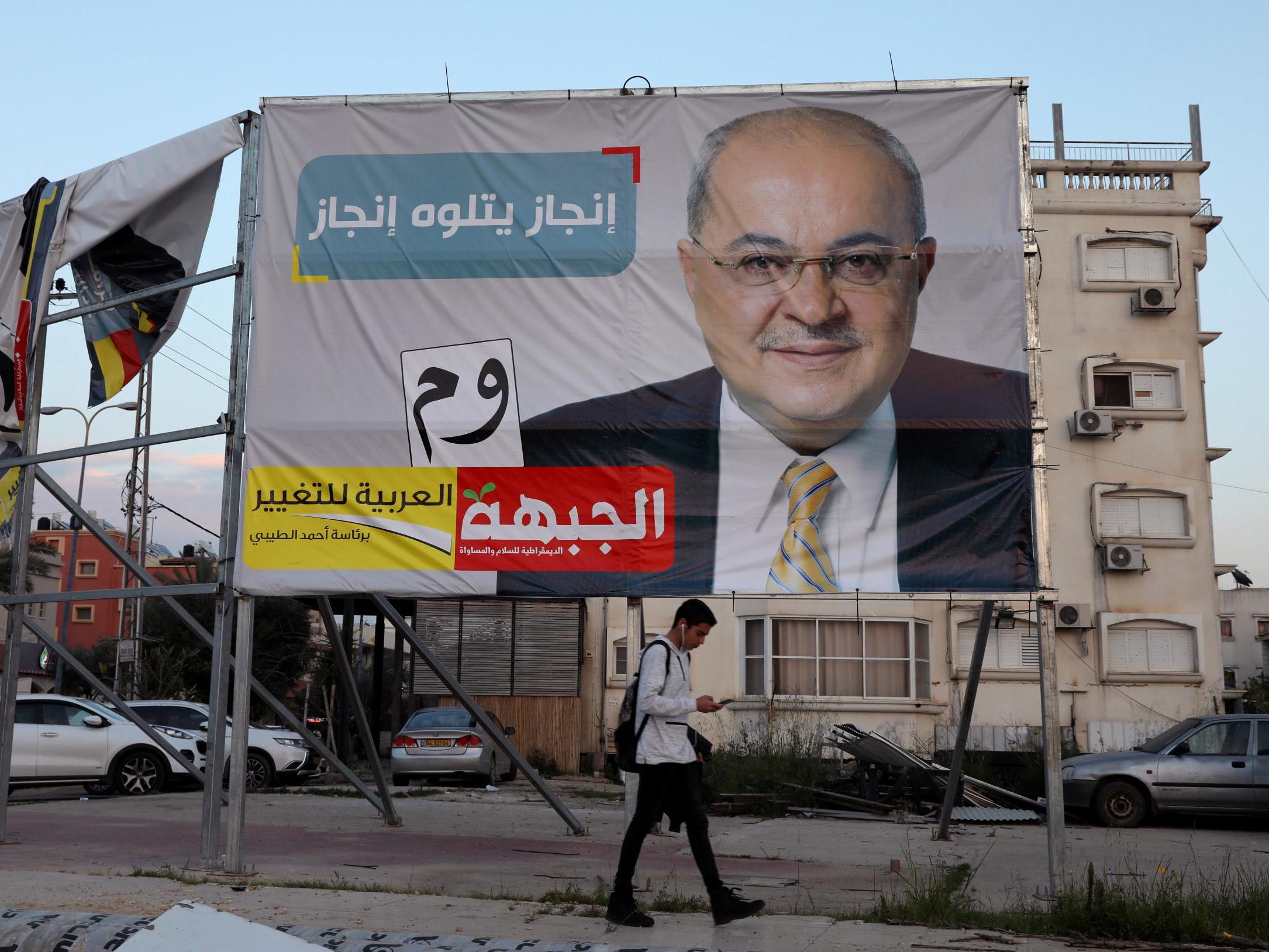 A youth walks past an Israeli election campaign banner depicting Ahmad Tibi, of the Hadash-Ta’al party in Taibe