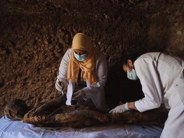 Two archaeologists examine a human mummy inside the tomb