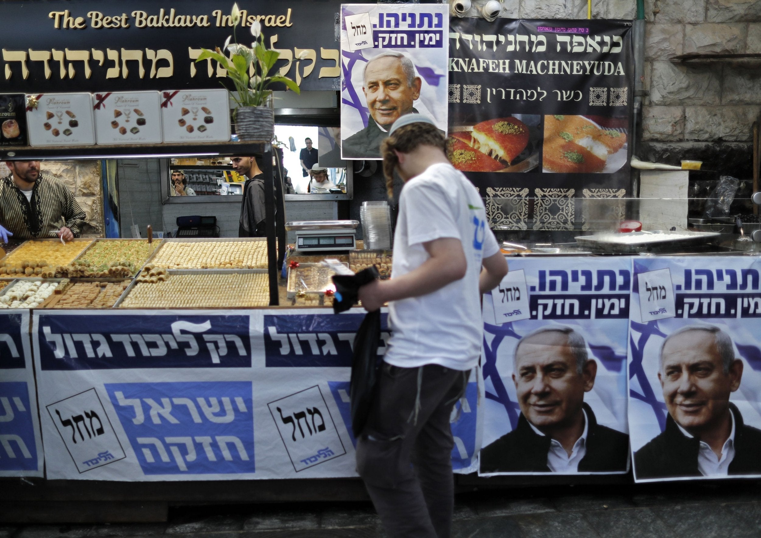 An Israeli settler walks past posters bearing the portrait of Israeli Prime minister Benjamin Netanyahu at the Machane Yehuda market in Jerusalem on April 8, 2019, a day ahead of the electoral polls