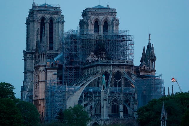 Firefighters (L and R) continue work to extinguish the fire at Notre Dame in Paris as dawn breaks on 16 April