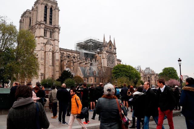 Onlookers stand on the banks of the Seine river in Paris on 16 April 2019 and view the aftermath of a fire at Notre Dame cathedral that caused its spire to crash to the ground.