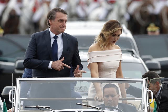 Jair Bolsonaro makes his trademark gun gesture as he rides in an open car with his wife after being sworn in as president in January