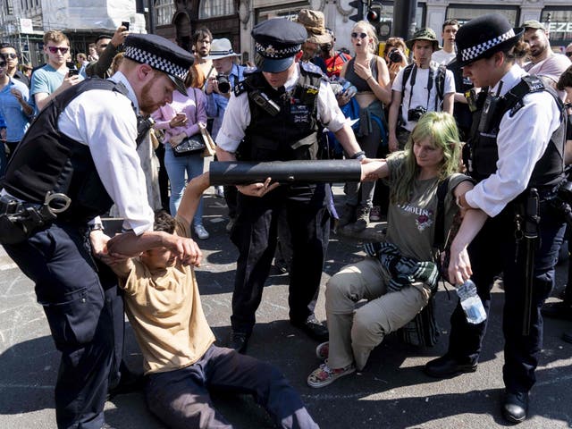 Police officers move activists with their hands glued to a pipe at Oxford Circus on 20 April