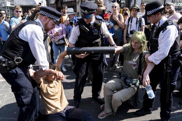 Police officers move activists with their hands glued to a pipe at Oxford Circus on 20 April