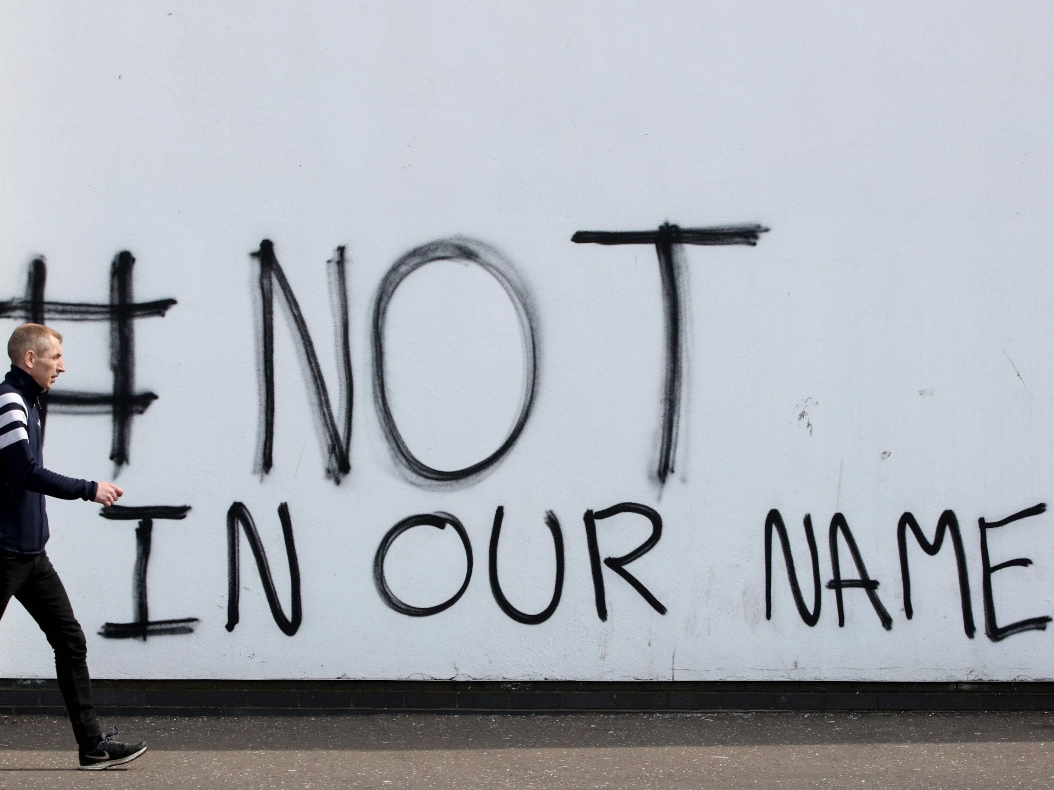A pedestrian walks past new graffiti that reads "# not in our name" in the Creggan area of Derry in Northern Ireland on 20 April 2019, near to where journalist Lyra McKee was fatally shot.