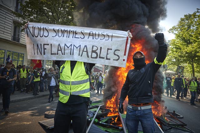 Gilets Jaunes stand in front of a burning barricade with a banner reading 'we can also burn' during widespread rioting