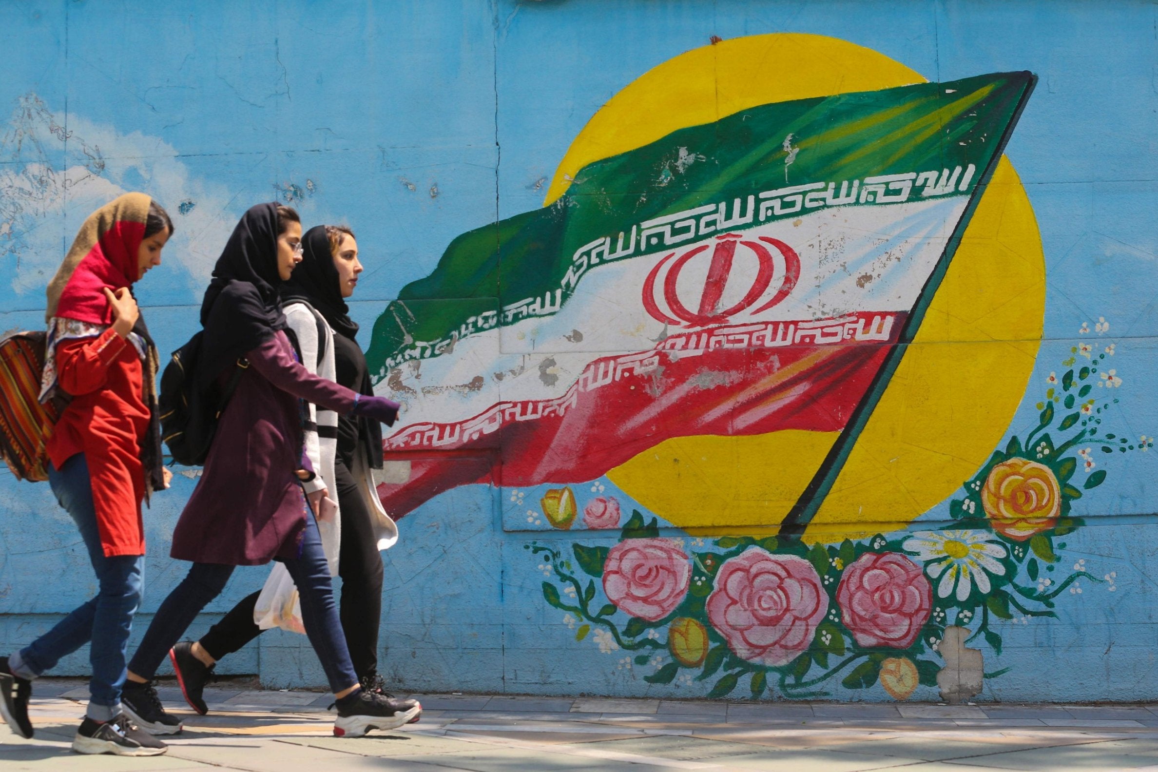 Young girls walk in front of a mural showing the Iranian national flag in the centre of the capital Tehran