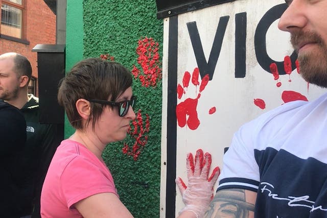 A friend of journalist Lyra McKee places a red paint handprint on the wall of a dissident republican office in Derry