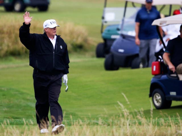 President Donald Trump waves to protesters while playing golf at Turnberry golf club