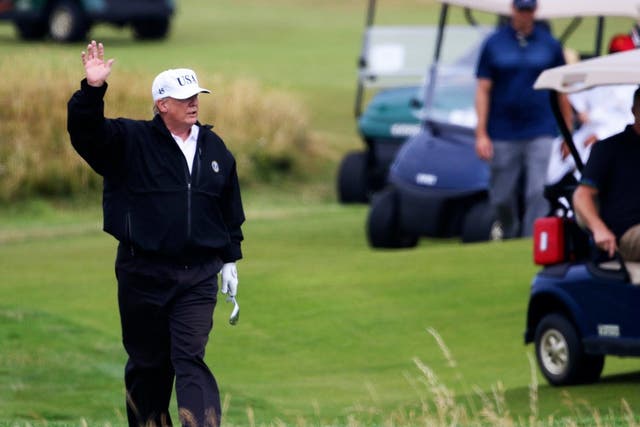 President Donald Trump waves to protesters while playing golf at Turnberry golf club