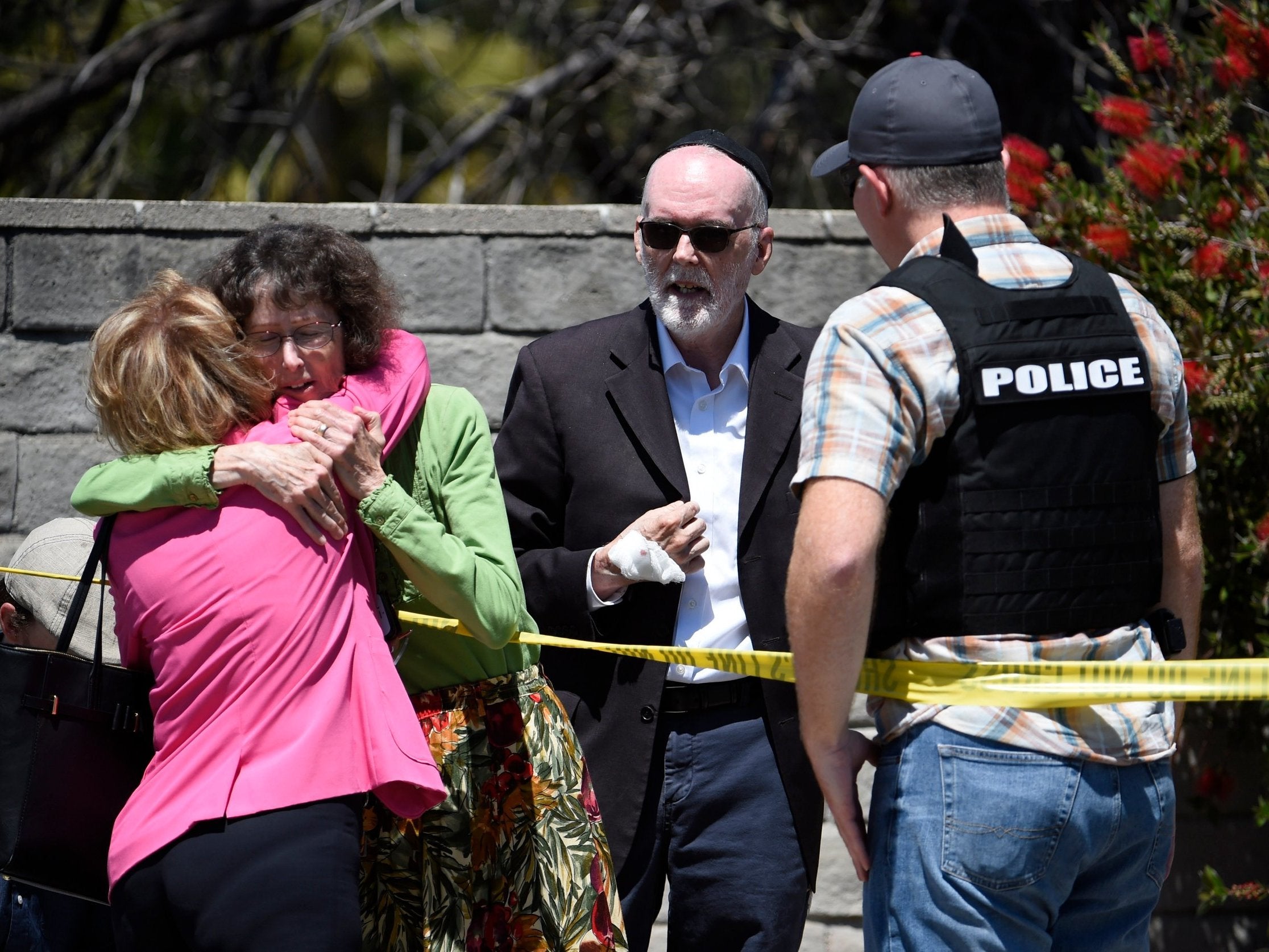 Two people hug as another talks to a police deputy outside of the Chabad of Poway Synagogue