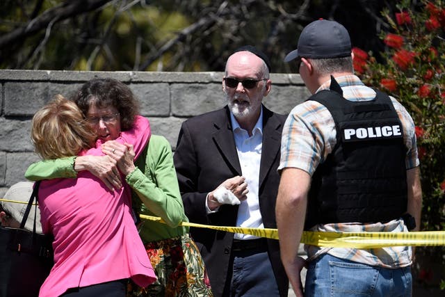 Two people hug as another talks to a police deputy outside of the Chabad of Poway Synagogue