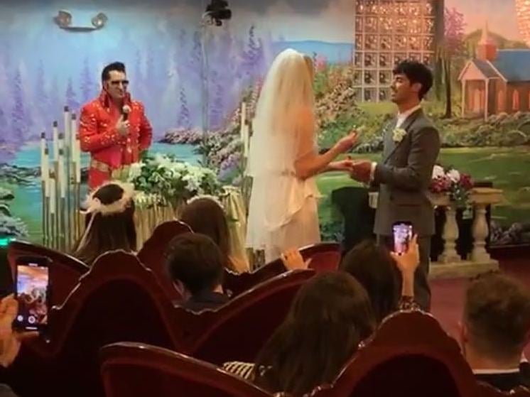 An Elvis Presley impersonator officiates as Sophie Turner and Joe Jonas place wedding rings on each other's fingers