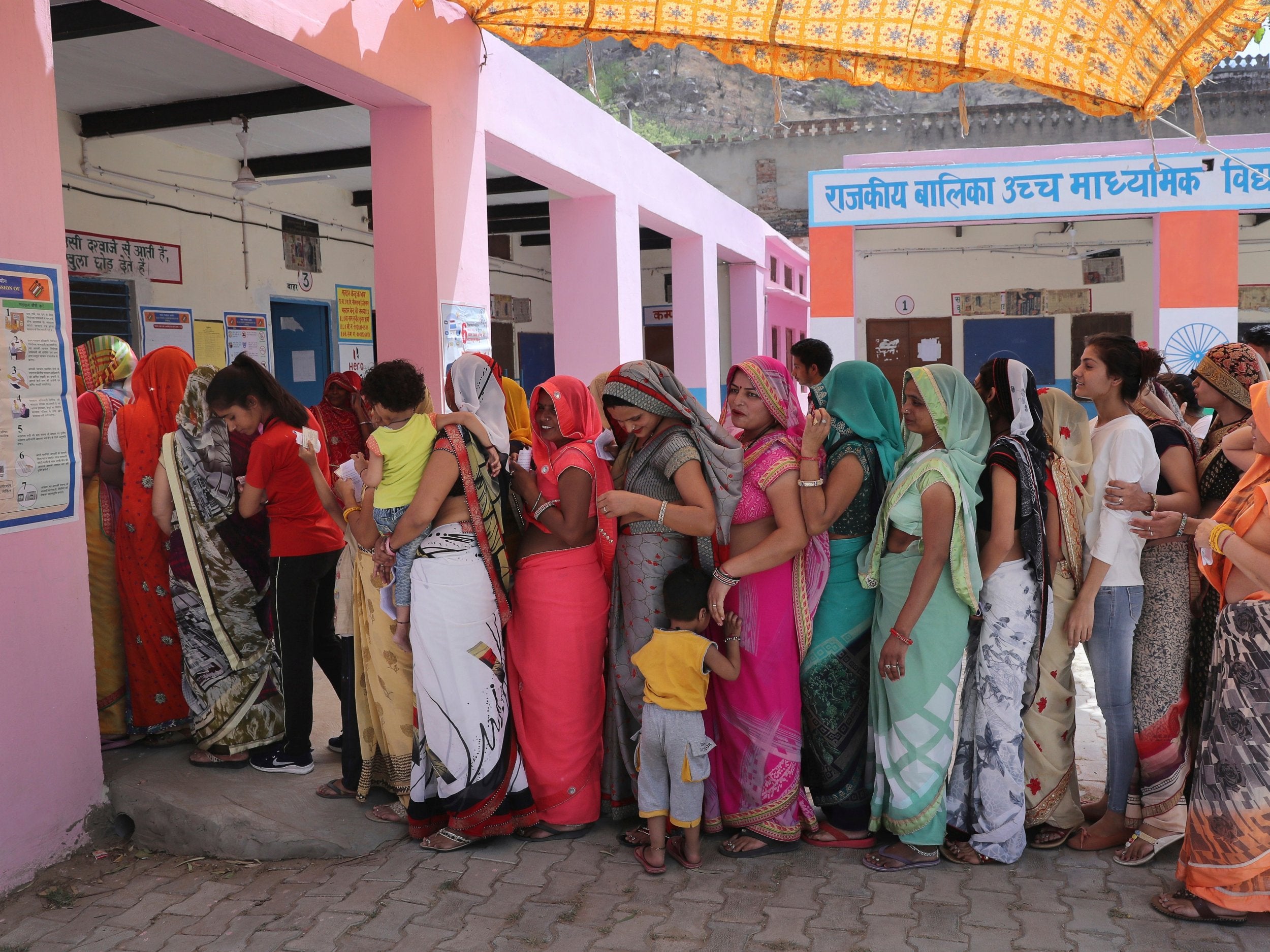 Indian women stand in a queue to cast their votes at a polling station in a village in Neemrana on Monday