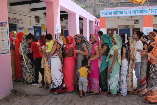 Indian women stand in a queue to cast their votes at a polling station in a village in Neemrana on Monday