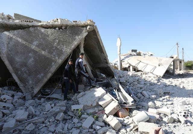 Syrians walk in the rubble of a bombed building in the village of Kansafrah, Idlib, on Tuesday