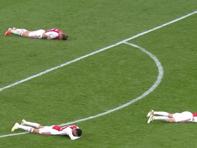 Ajax players lie dejected on the ground as Tottenham celebrate their last-gasp winner